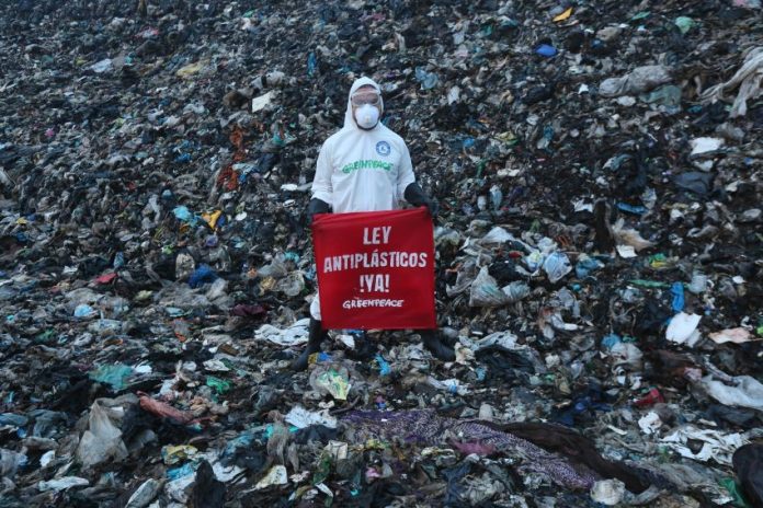 A member of Greenpeace Mexico stands on a mountain of trash at the Coatzacoalcos landfill wearing a hazmat suit with a sign reading 