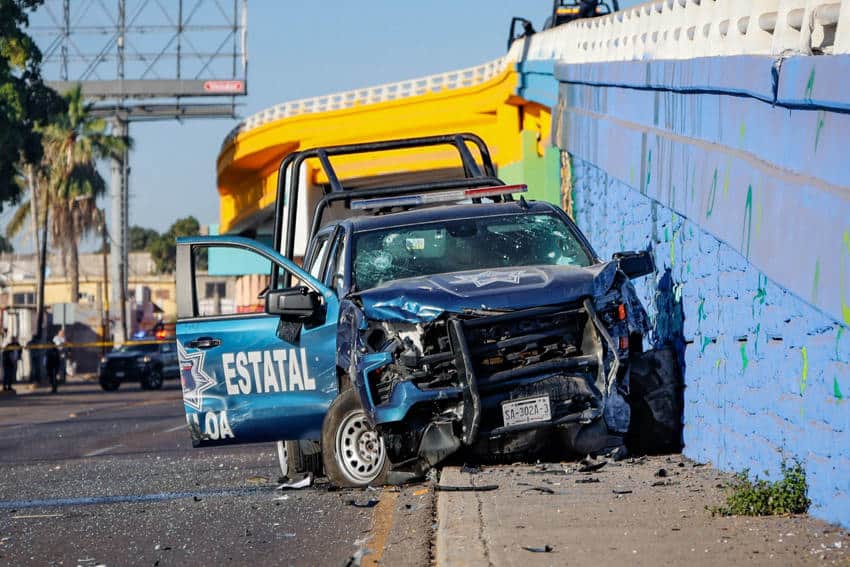 A state police pickup truck from Culiacan, Mexico, with a crushed grill and destroyed headlights. The truck is parked half on the sidewalk and half on the street.