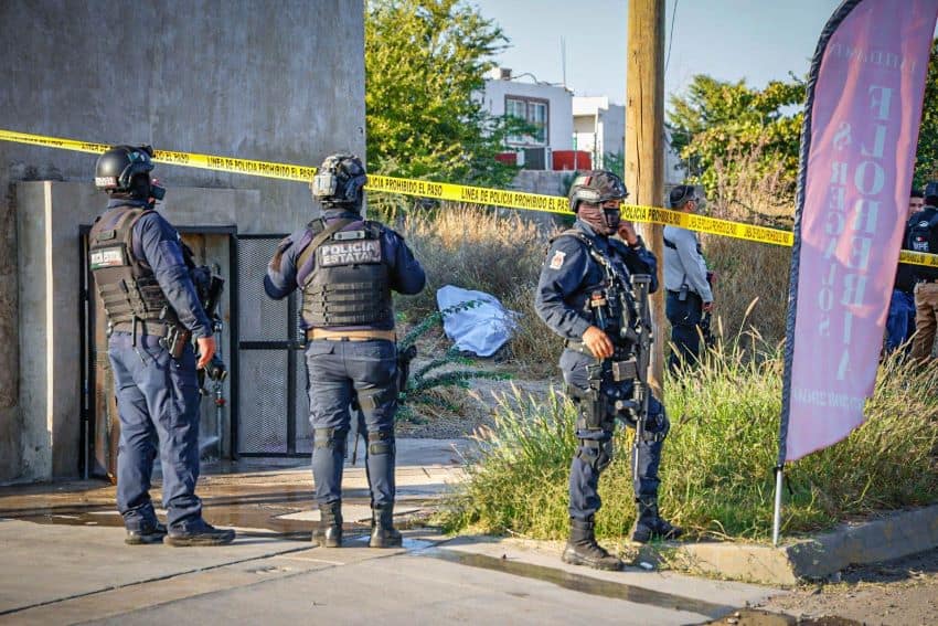 Masked and heavily armed police officers stand near a taped-off crime scene in Culiacán, Sinaloa, as Security Minister Omar García Harfuch inspects the area.