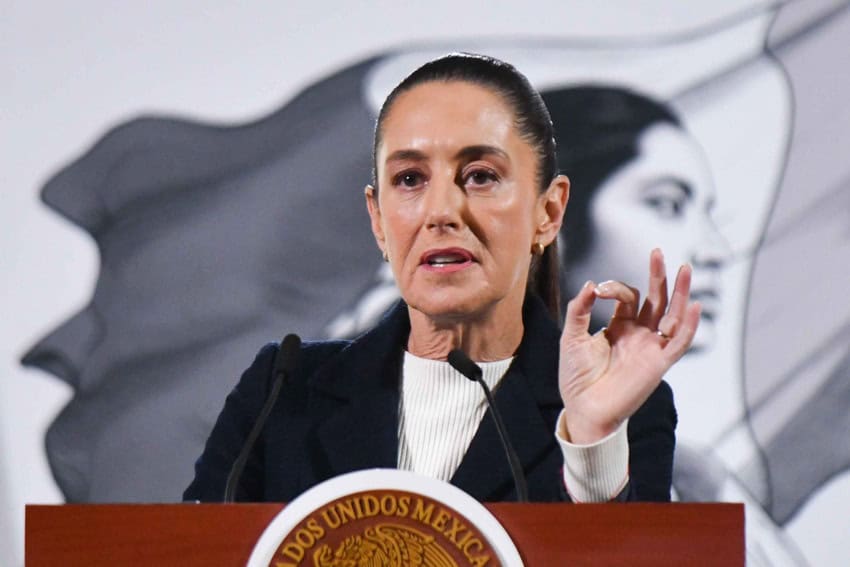 Mexican President Claudia Sheinbaum standing at the presidential podium during a press conference at the National Palace emphasizing her point with a hand up and her thumb and forefinger pressed together in an oval.