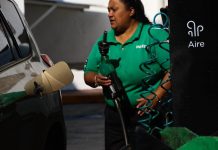 Mexican woman wearing Pemex uniform holding a gas station pump as she prepares to put it into a car's gas tank.