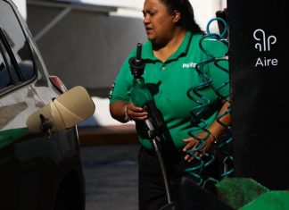 Mexican woman wearing Pemex uniform holding a gas station pump as she prepares to put it into a car's gas tank.