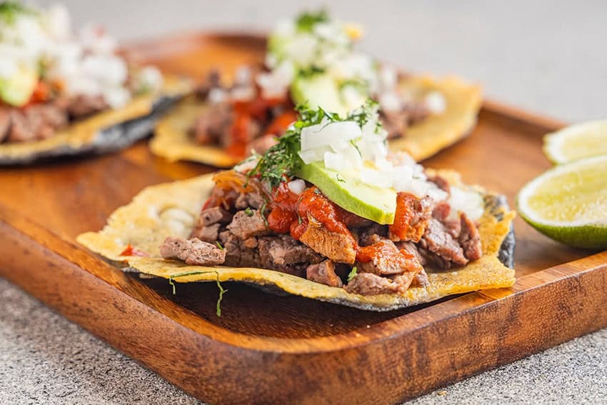 A gourmet taco de asada served on a wood cutting board with lime and cilantro