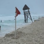 People in the water on a Cancun beach. On the beach near the shore is a red advisory flag warning of strong currents