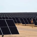 Thousands of solar panels in rows at an angle facing up at the sky in a desert area of Sonor