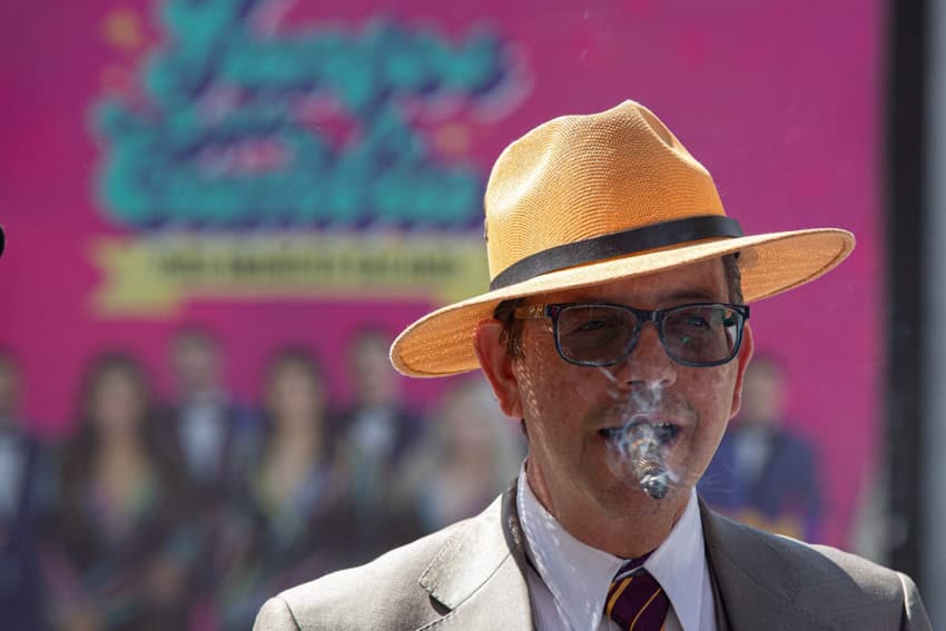 Man wearing a suit and tie, a straw fedora hat and sunglasses and smoking a cigar on the streets of Mexico City