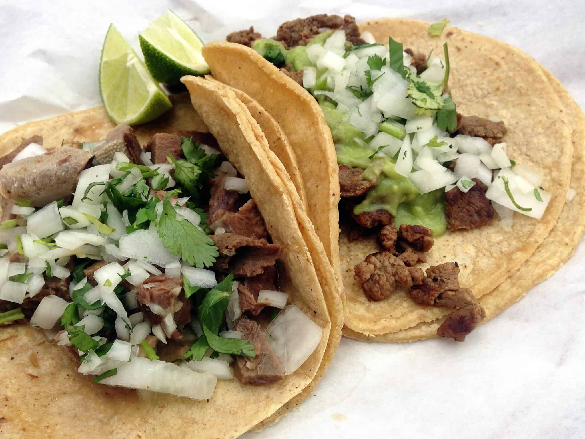 A plat of tacos de asada served with chopped onion, cilantro and lime on corn tortillas