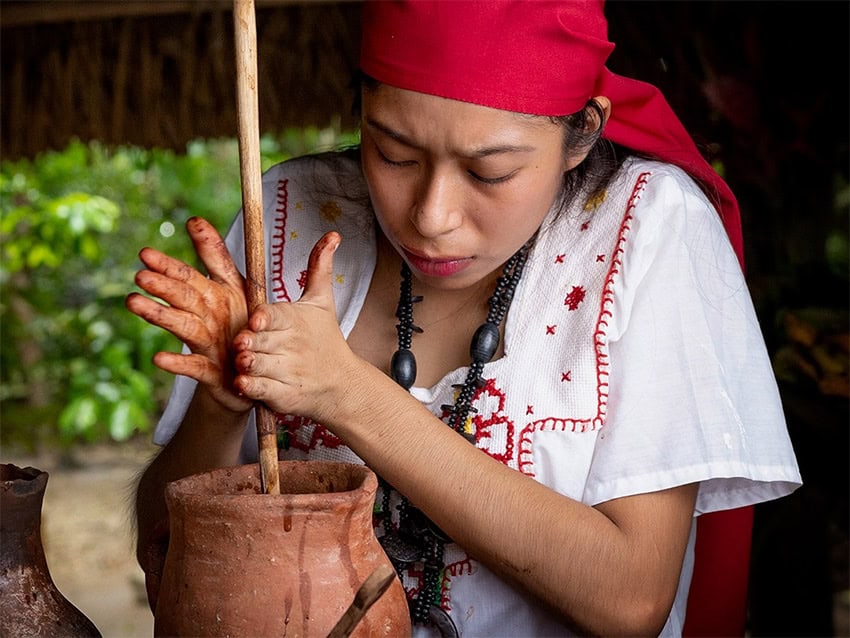 A woman grinds cacao into chocolate in a clay pot in Tabasco