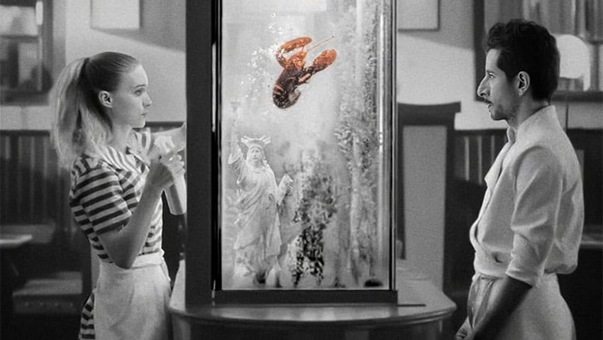 An image shows a man and woman looking at each other from opposite sides of a lobster tank, a still from the 2024 movie La Cocina