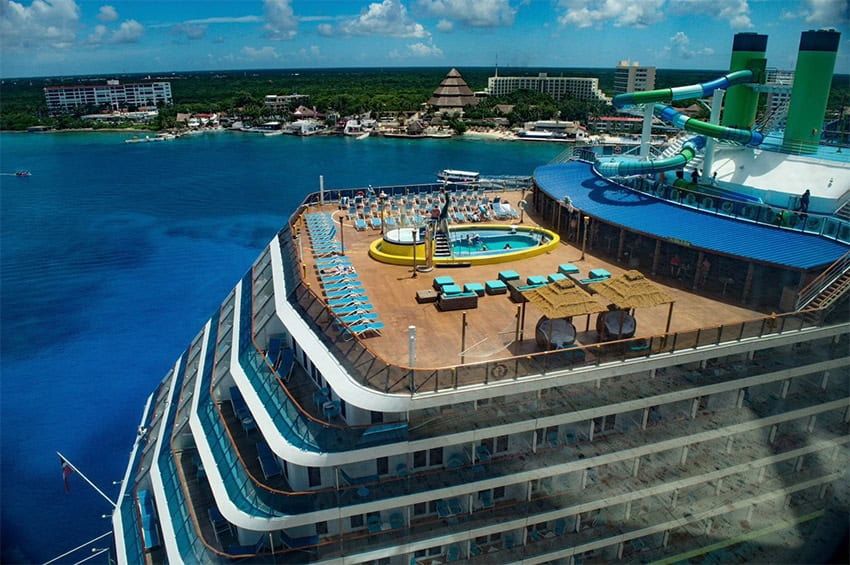 An aerial photo shows the deck of a large cruise ship with the island of Cozumel visible in the background