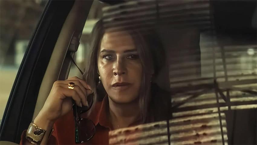 A woman looks pensive, seen through a car windshield, which reflects city lights