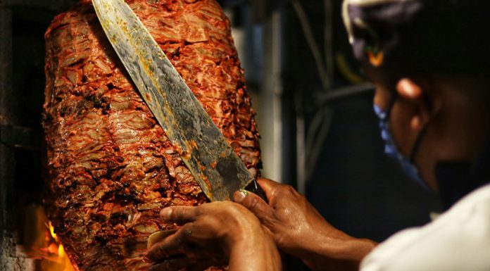 A taquero cuts meat of a trombo of al pastor taco meat.