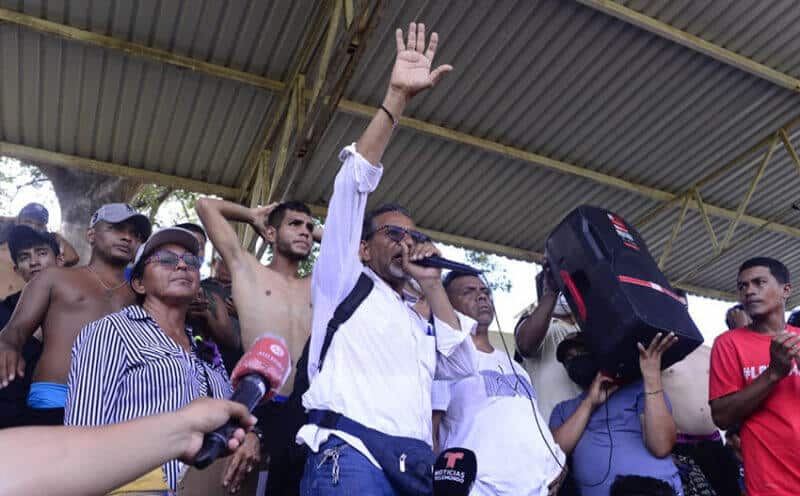 Pastor and migrant advocate Luis Rey García Villagrán shouts into a microphone in a crowded area shaded by a tin roof