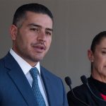 Security Minister García Harfuch speaks at a microphone while Presiden Sheinbaum stands nearby