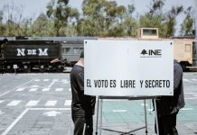 A Mexican voter fills out a ballot in a voting booth bearing the words "INE" and "El voto es libre y secreto."