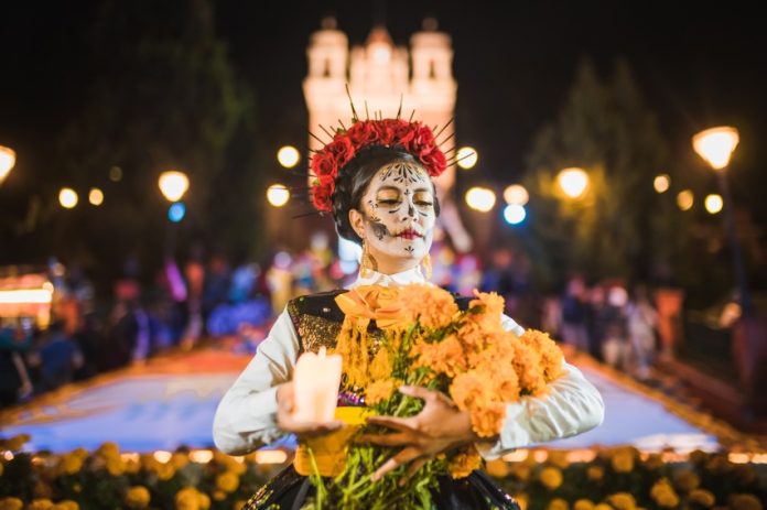 Mexican woman dressed as a Catrina and in white skeletal makeup holding Mexican marigolds