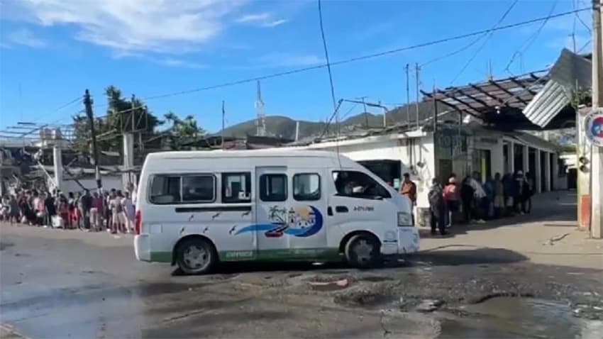 A long line of people wait at a minibus stop.