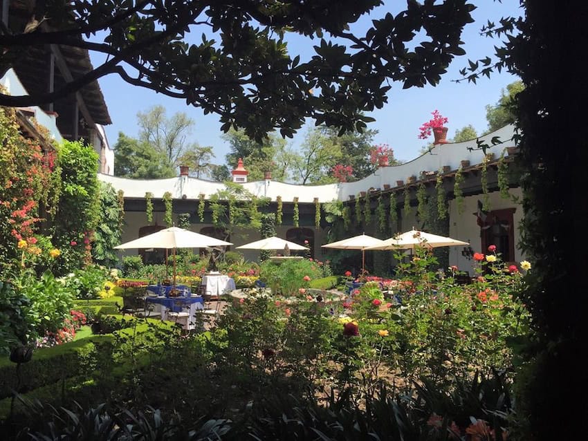 Side view from inside the San Angel Inn hacienda of the main patio, decorated with different flowers that give life to the patio, in the center there are some tables from the hacienda restaurant.